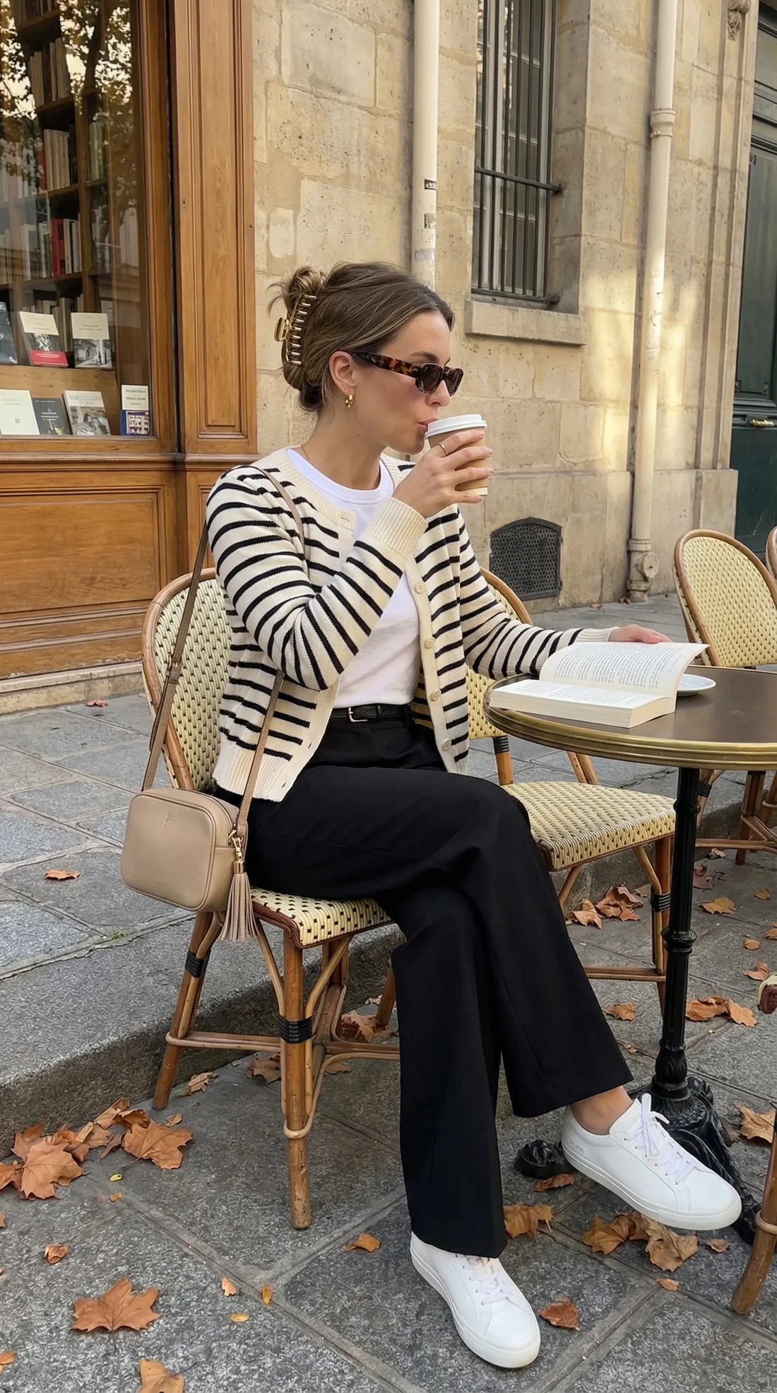 Outfits for Paris in fall: striped cardigan, white tee and black wide-leg trousers at a Paris café table